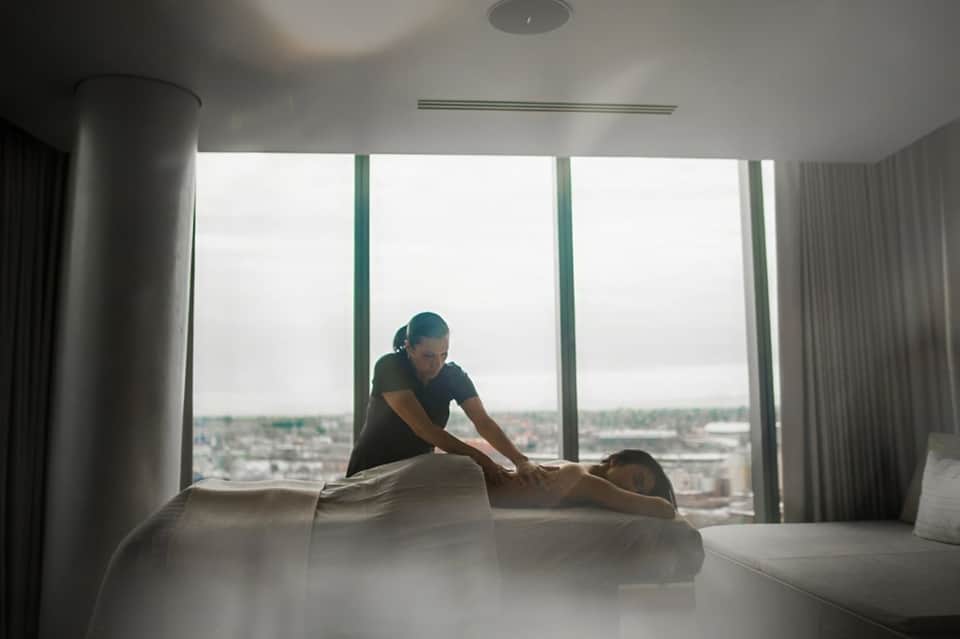 Massage therapist performing treatment on client in high-rise spa room with city skyline view