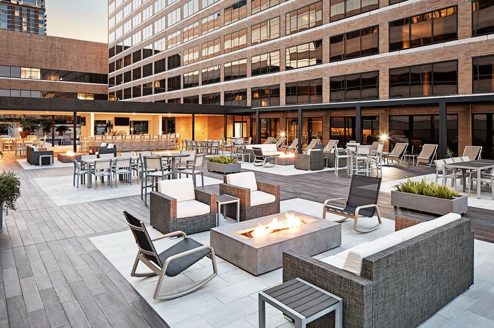 Upscale rooftop terrace with fire pit, lounge seating, and modern high-rise buildings at dusk