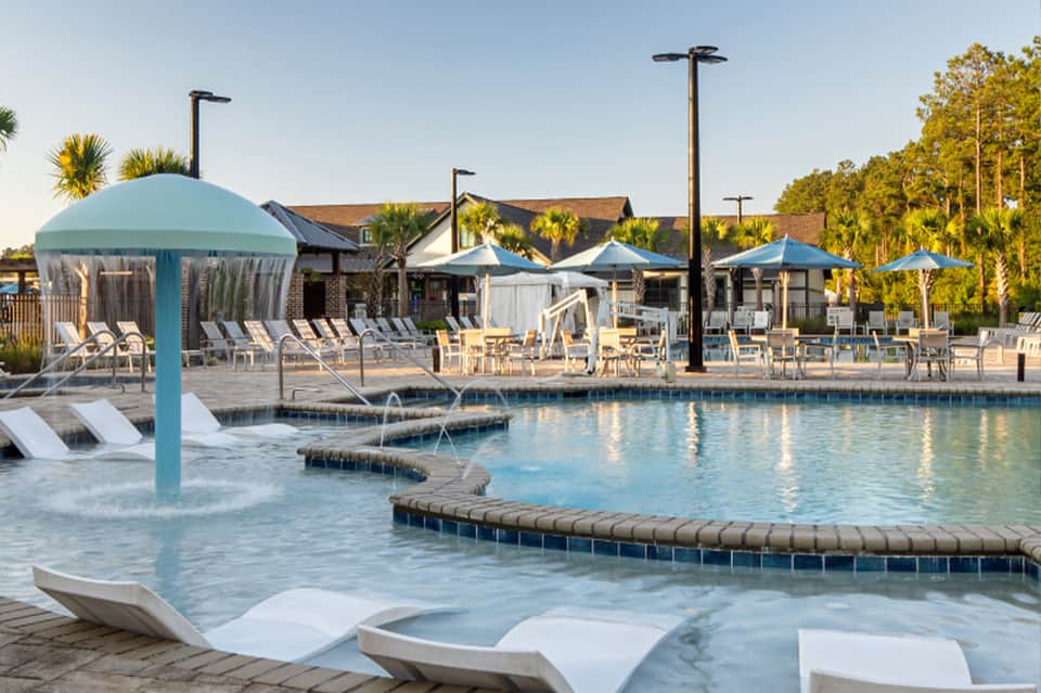 Resort pool area with turquoise water, teal umbrellas, lounge chairs, and spa buildings