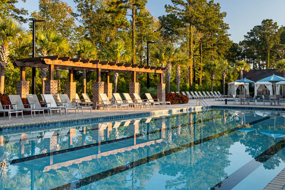 Resort pool with yellow pergola, lounge seating, umbrellas, and palm trees lining property