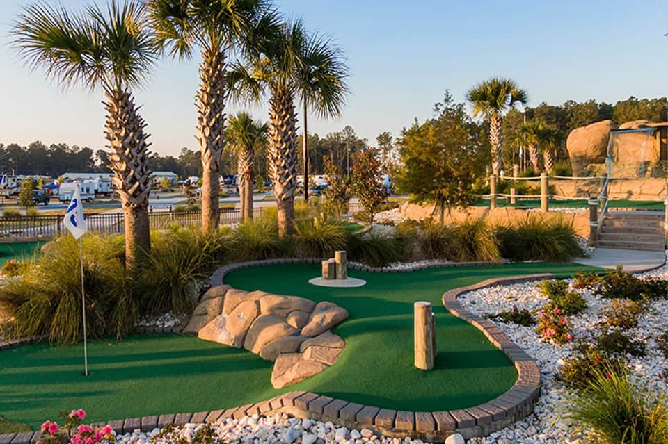 Miniature golf course with artificial green, rock formations, palm trees, and water features in recreational setting