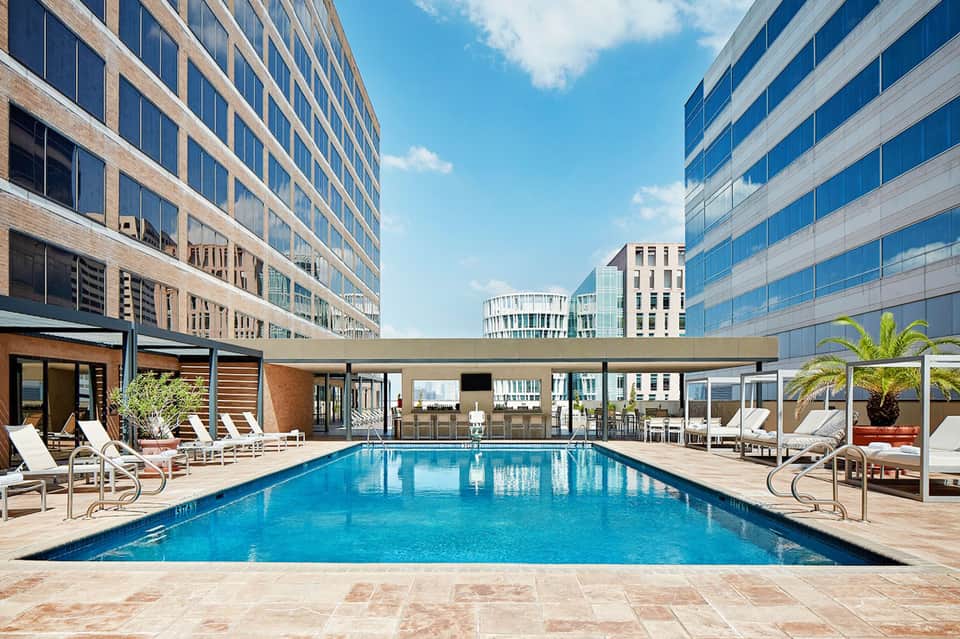 Luxury rooftop pool surrounded by high-rise buildings with lounge chairs and palm trees