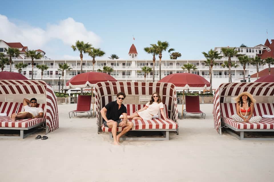 Beachfront cabanas with red and white striped canopies, hotel building with tower, and guests relaxing