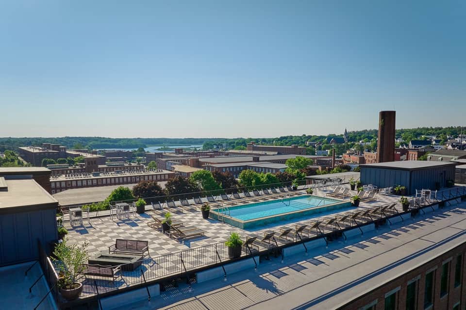 Rooftop swimming pool with blue water overlooking industrial cityscape and distant waterfront