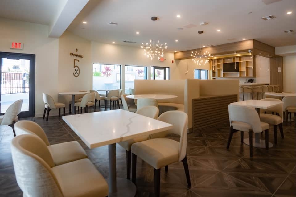 Hotel lobby lounge with modern furnishings, wooden accents, pendant lighting, and dining tables