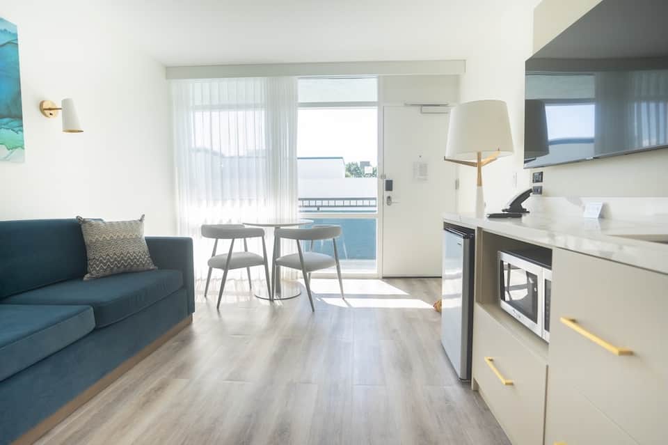 Modern studio apartment with kitchenette, blue sofa, dining area, and ocean-view balcony