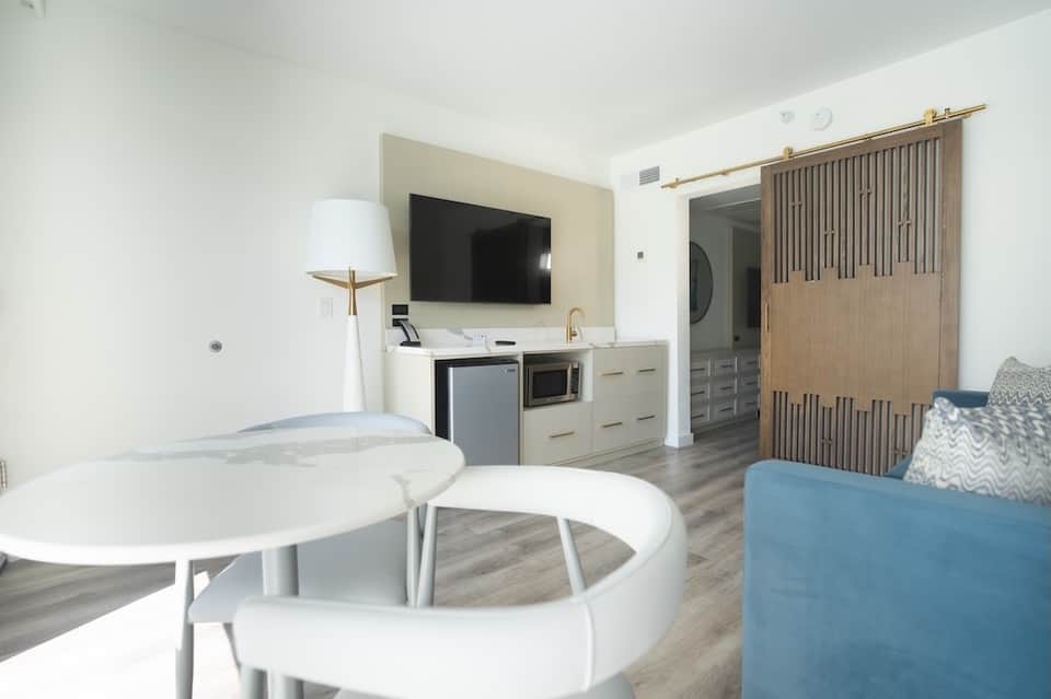 Modern hotel suite with TV, kitchenette, seating area, and wooden barn doors