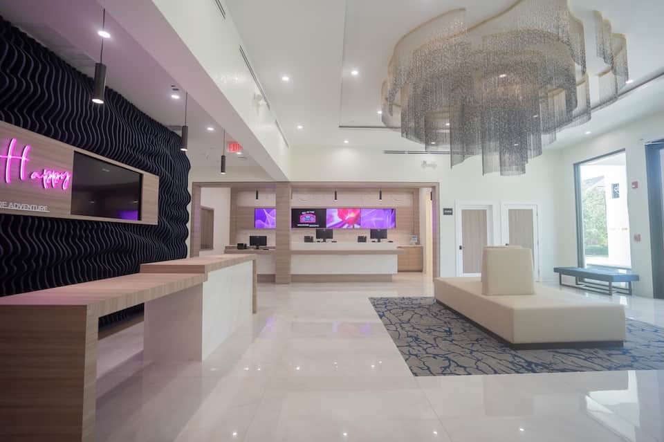 Modern hotel lobby with pink neon signage, reception desk, and contemporary light fixture