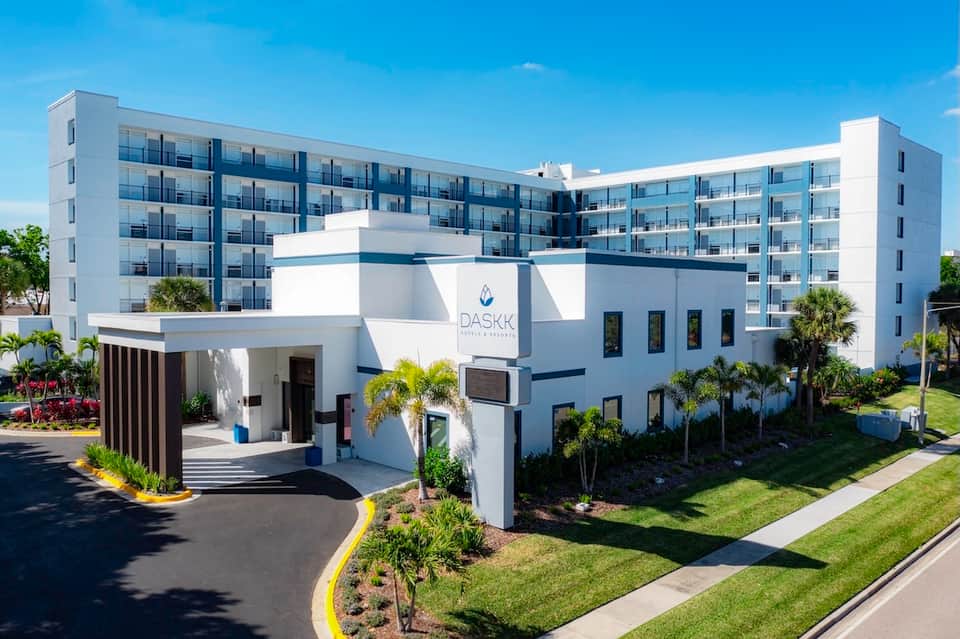 Modern white resort building with entrance, palm trees, and manicured grounds