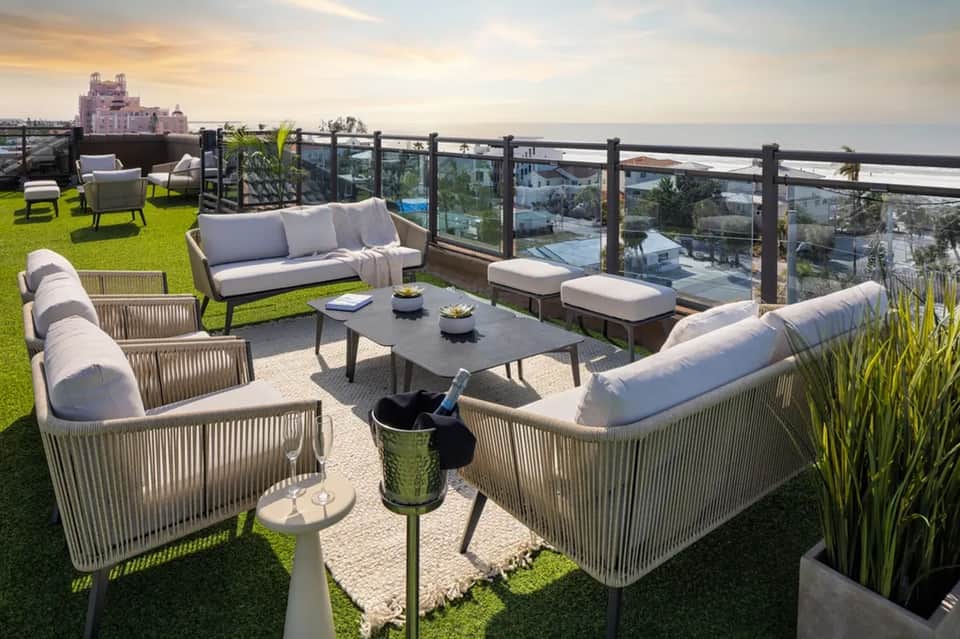 Luxury rooftop terrace with lounge seating, ocean views, manicured lawn, and glass railing
