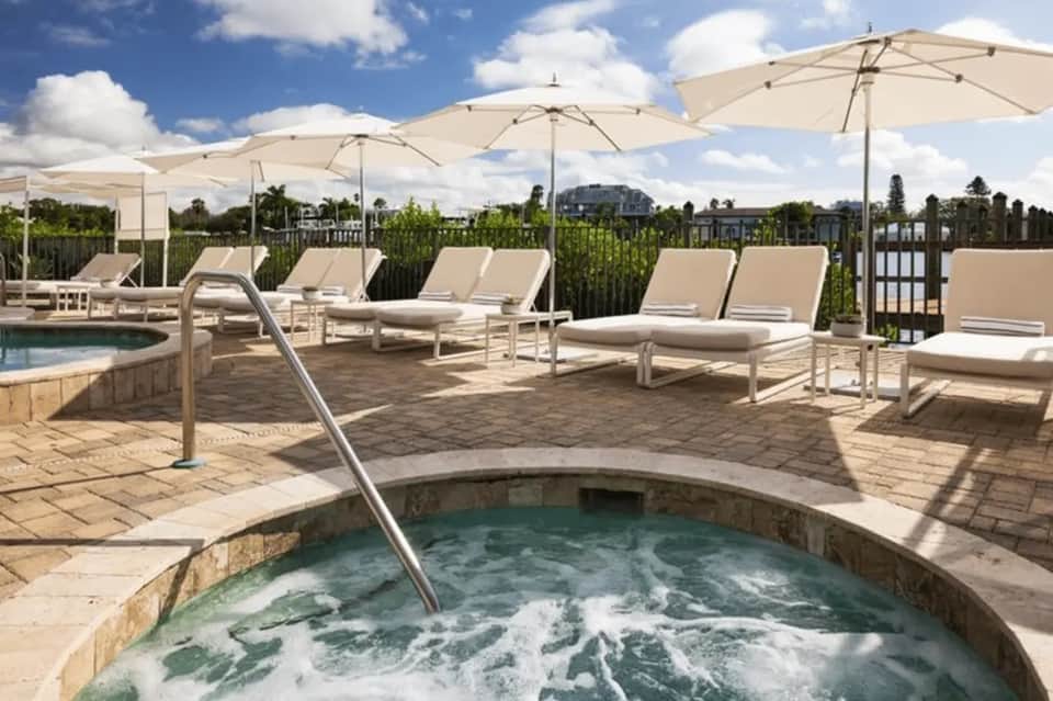 Resort rooftop with hot tub, lounge chairs under umbrellas, and panoramic views of surrounding landscape