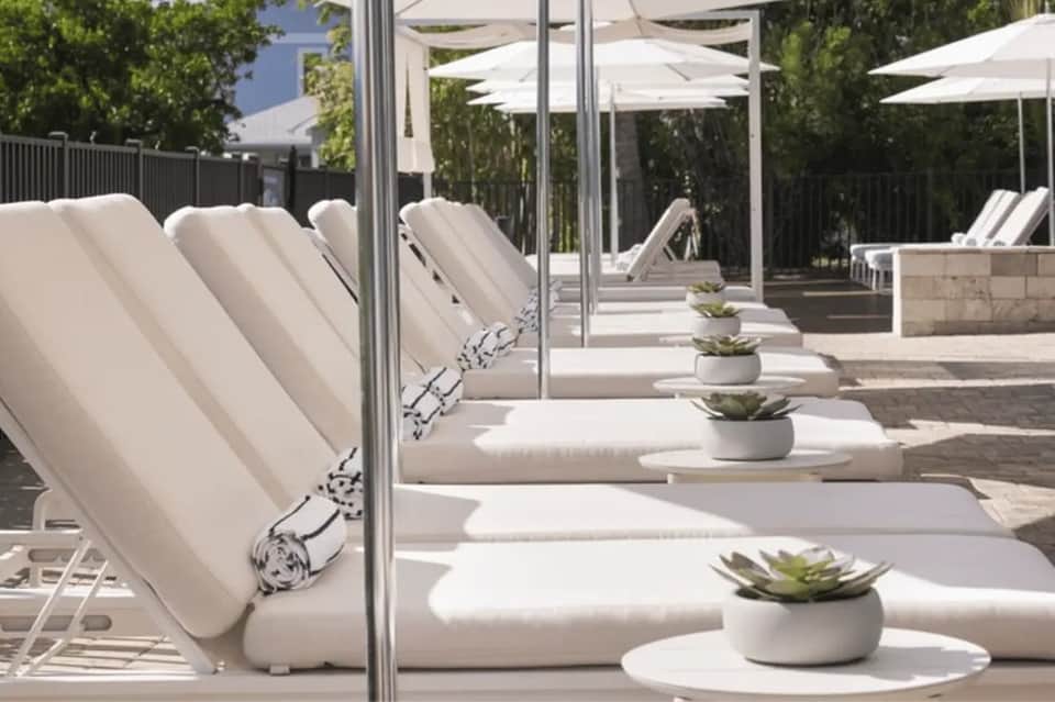 Outdoor spa lounge with white cushioned loungers, rolled towels, succulents, umbrellas, and pergola pergola seating area