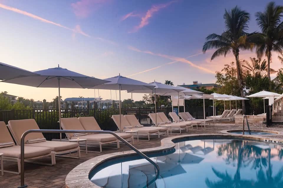 Resort pool at sunset with lounge chairs, umbrellas, and palm trees