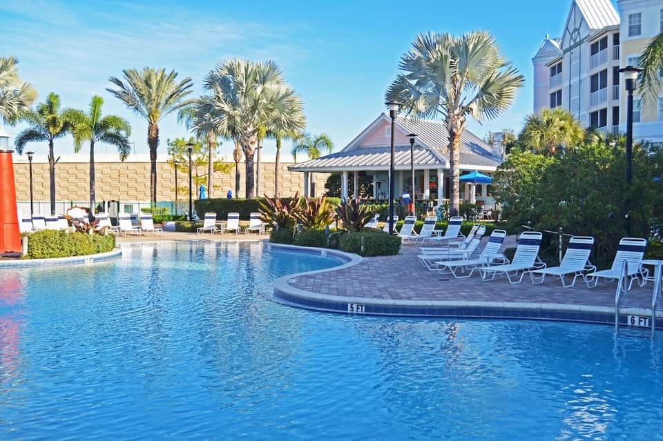 Resort pool surrounded by palm trees, lounge chairs, tropical vegetation, and white gazebo