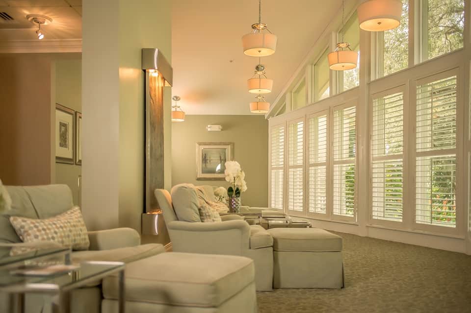 Wellness relaxation room with comfortable seating, green walls, pendant lighting, and large shuttered windows