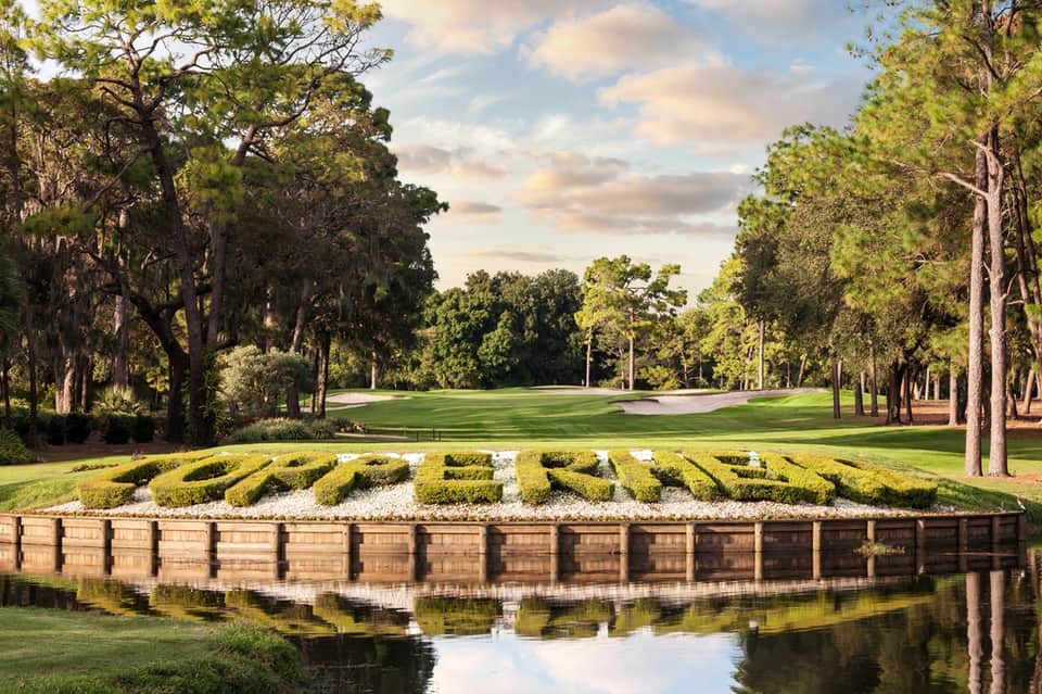 Golf course with manicured green, trees, bunker, and water feature reflection