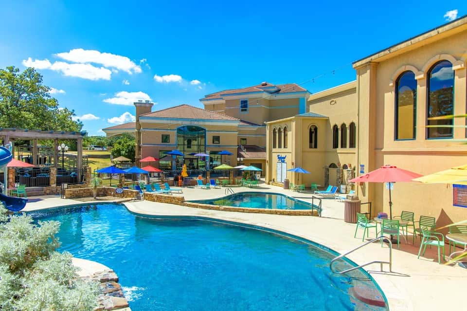 Resort pool complex with blue water, colorful umbrellas, architectural buildings, and landscaping