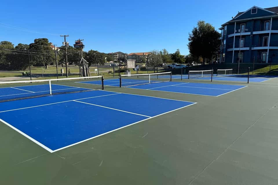 Community pickleball courts with blue and green playing surfaces, white nets, and residential buildings