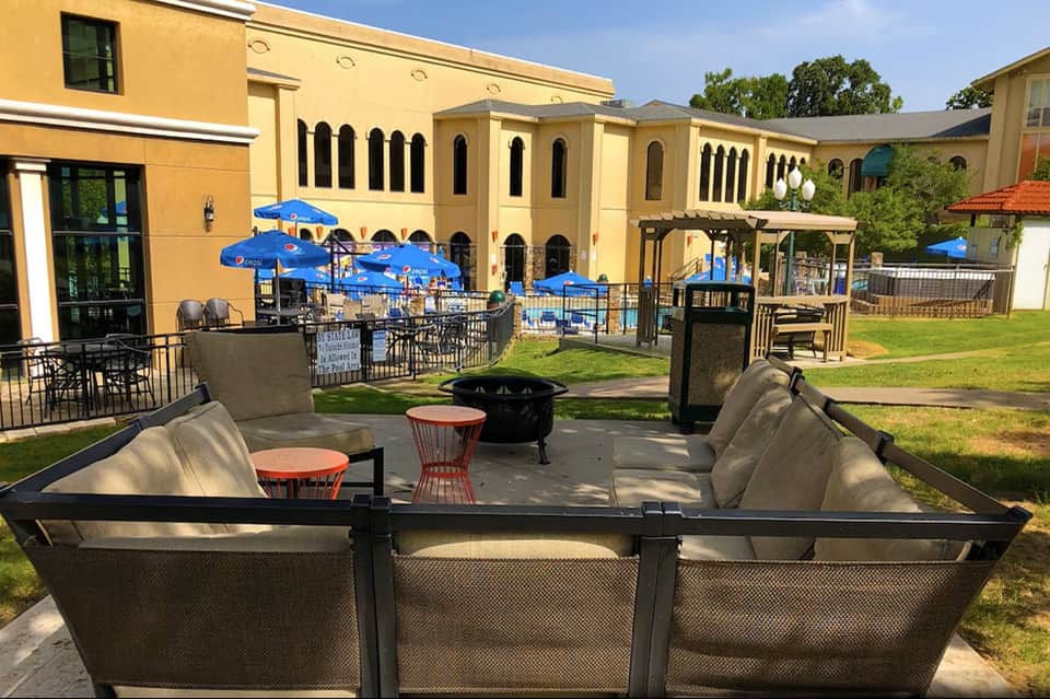Resort courtyard with lounge seating, fire pit, blue umbrellas, and yellow Spanish colonial-style buildings