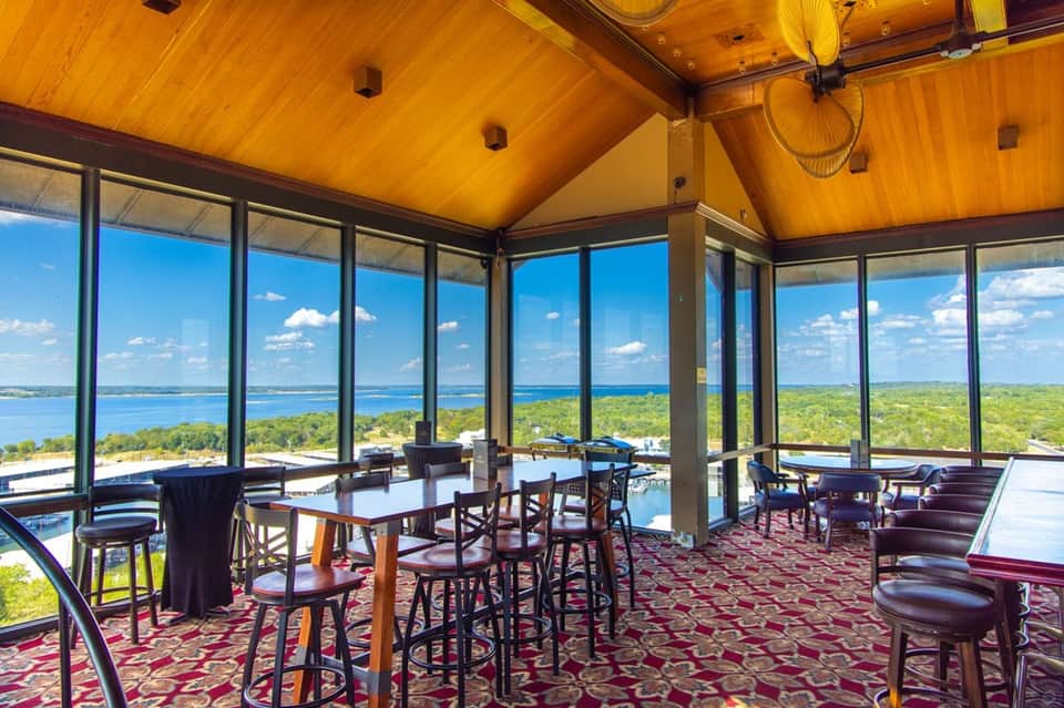 Glass-enclosed event space with panoramic lake and landscape views, wooden ceiling, dining tables