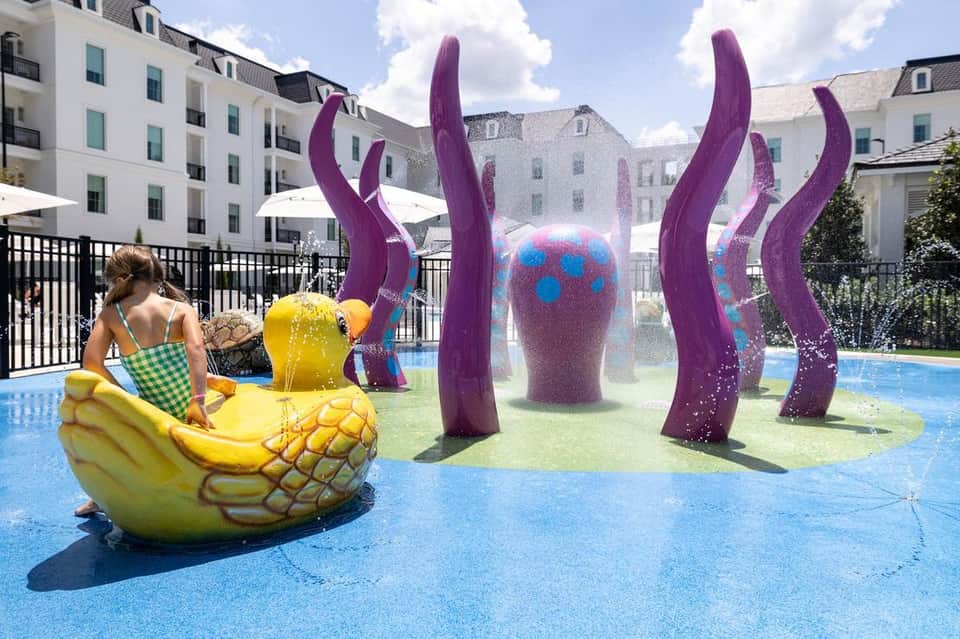 Children's pool area with colorful purple sculptural installations and splash pad features