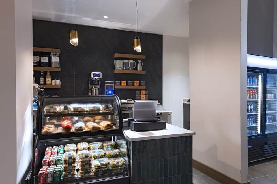 Contemporary café counter with pastry display case, espresso machine, shelving, and beverage refrigerators