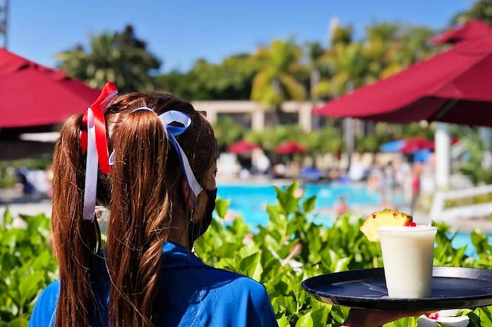 Girl with ribbons in hair overlooking resort pool with red umbrellas and tropical landscaping