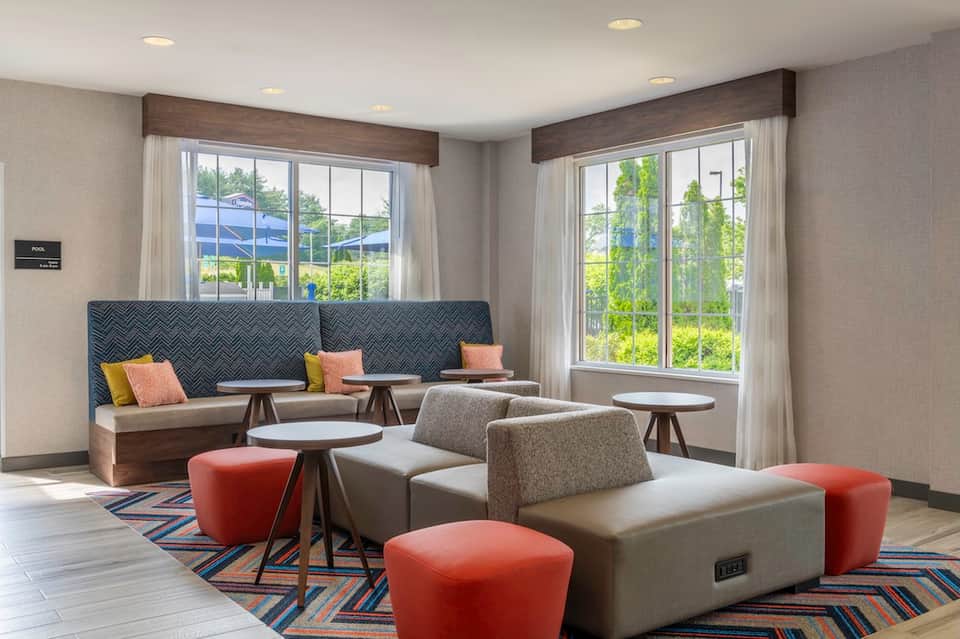 Modern lounge with patterned banquette seating, side tables, colorful pillows, and floor-to-ceiling windows