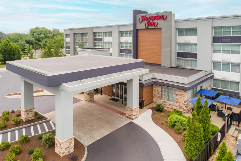 Modern Hampton Inn hotel exterior with covered entrance and outdoor seating area