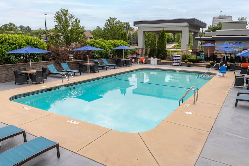 Modern resort pool with sun loungers, blue umbrellas, shade structures, and landscaping