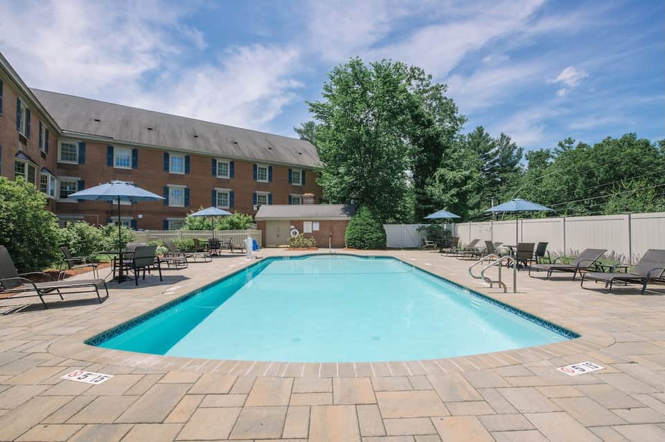 Resort outdoor pool with lounge chairs, umbrellas, brick building, and manicured landscaping