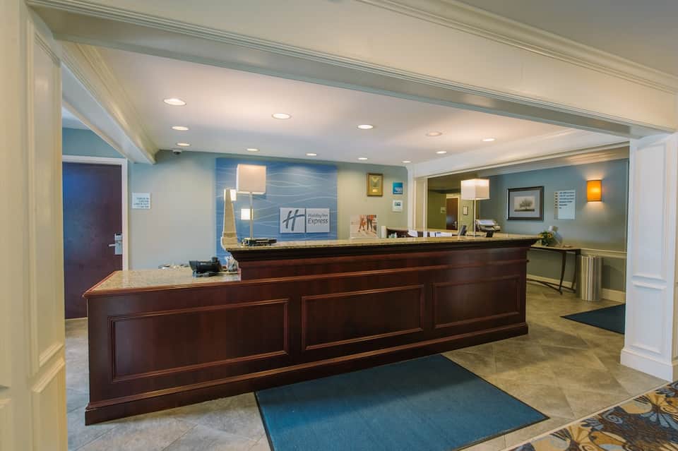 Hotel lobby with dark wood reception desk, blue walls, recessed lighting, and traditional furnishings