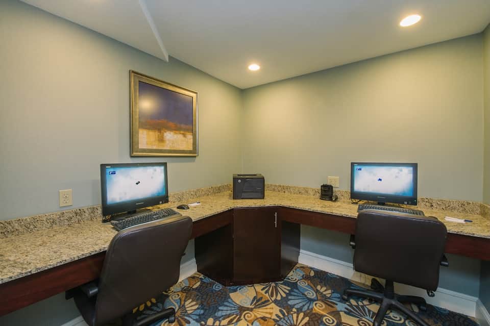 Hotel business center with curved granite desk, two computer monitors, chairs, and framed artwork