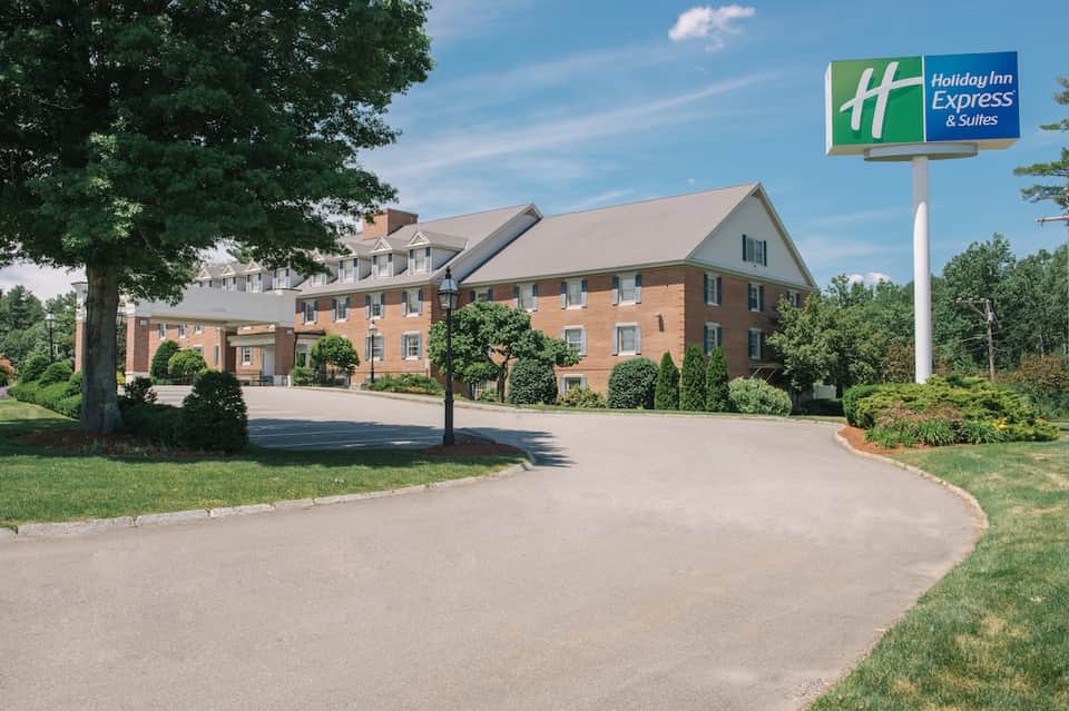Holiday Inn Express & Suites brick building exterior with sign, driveway, landscaping, and trees