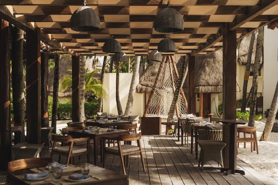 Outdoor dining pergola with woven pendant lights, palm trees, and casual restaurant seating