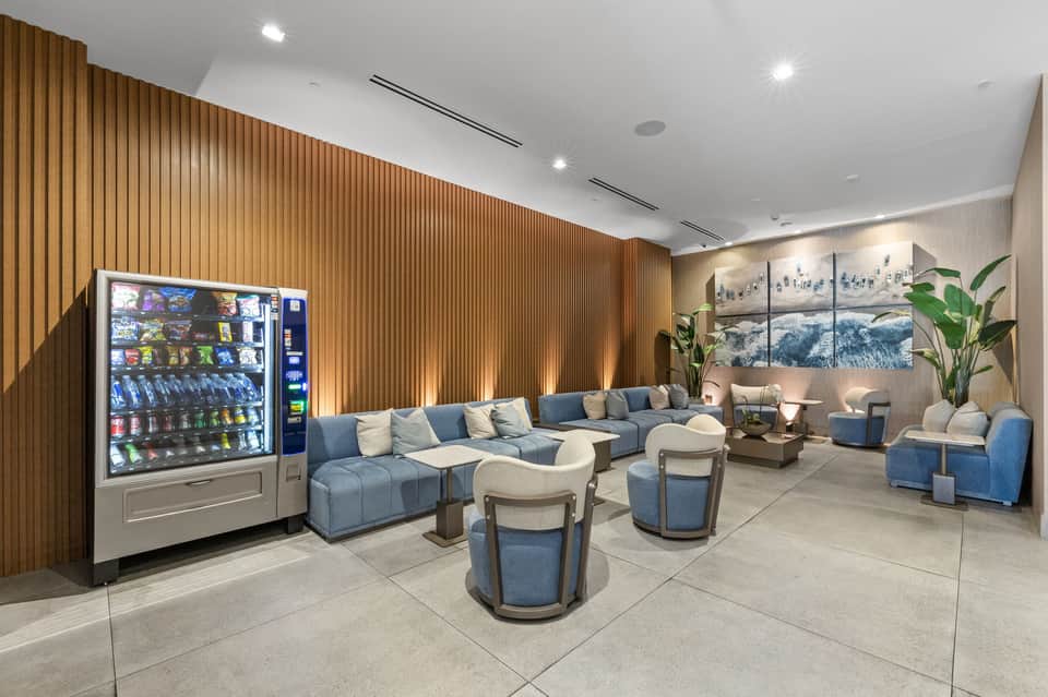 Modern hotel lobby lounge with blue seating, vending machine, wood paneling, and landscape art