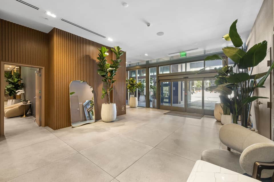 Contemporary hotel lobby with wood paneling, plants, marble flooring, and glass entrance doors