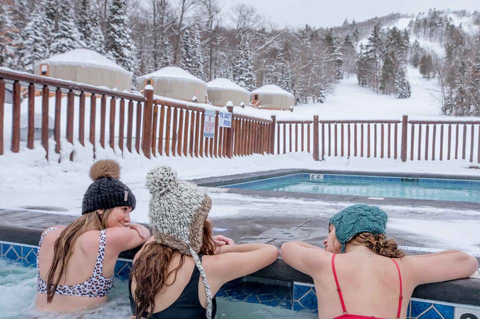 Group enjoying hot tub in snowy mountain setting with winter landscape and ski runs visible