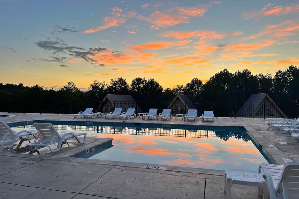 Resort swimming pool at sunset with lounge chairs, cabanas, and colorful sky reflection in water