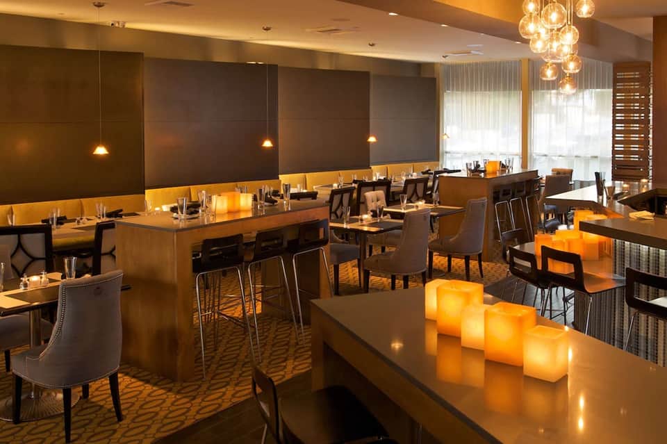 Restaurant dining room with wood bar, modern lighting, and amber-colored candles