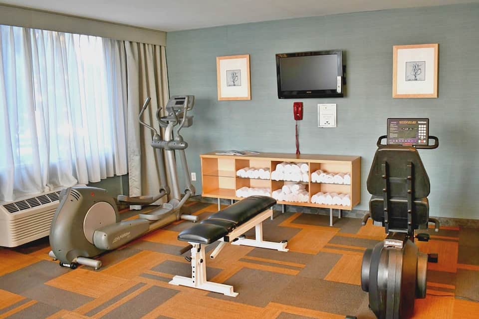 Fitness center with cardio equipment, dumbbells, workout bench, and light blue accent wall with windows