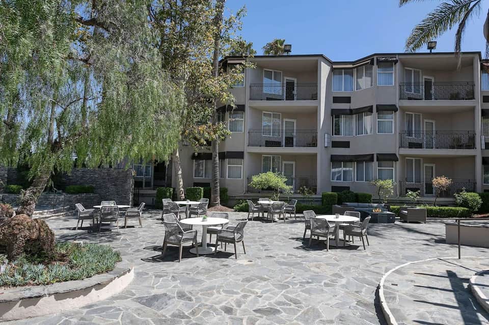 Resort courtyard with casual seating area, stone patio, landscaping, and multi-story building