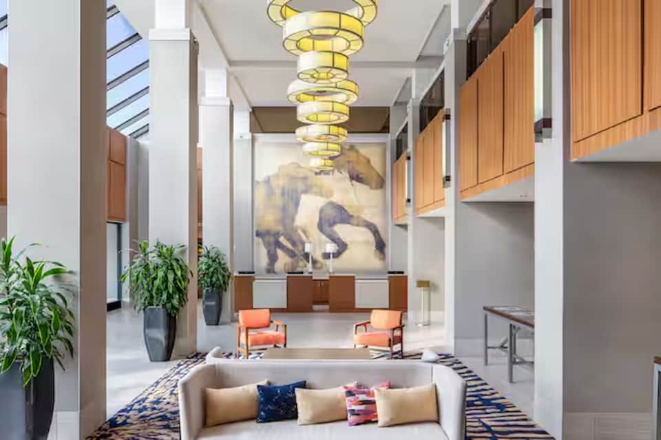 Modern hotel corridor with spiral yellow chandelier, white columns, artwork, and contemporary seating