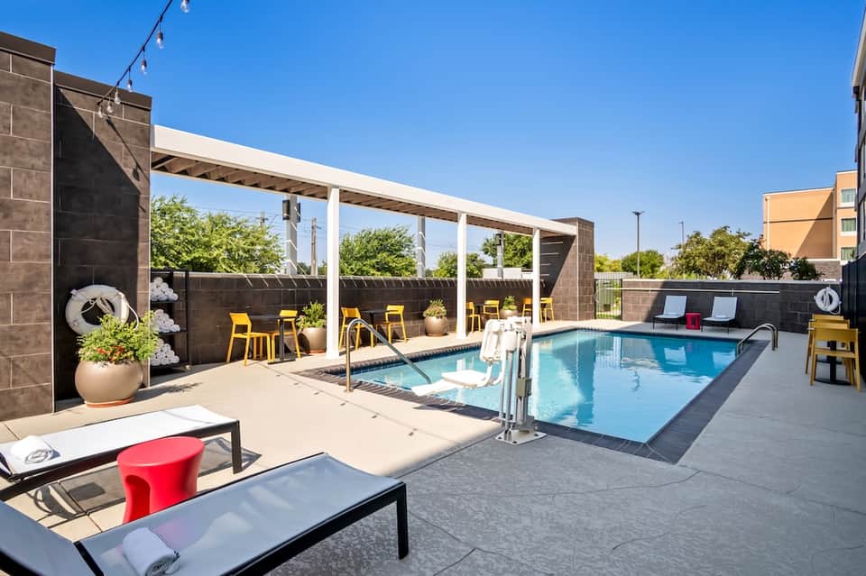 Rooftop pool deck with blue swimming pool, loungers, pergola, and yellow accent chairs