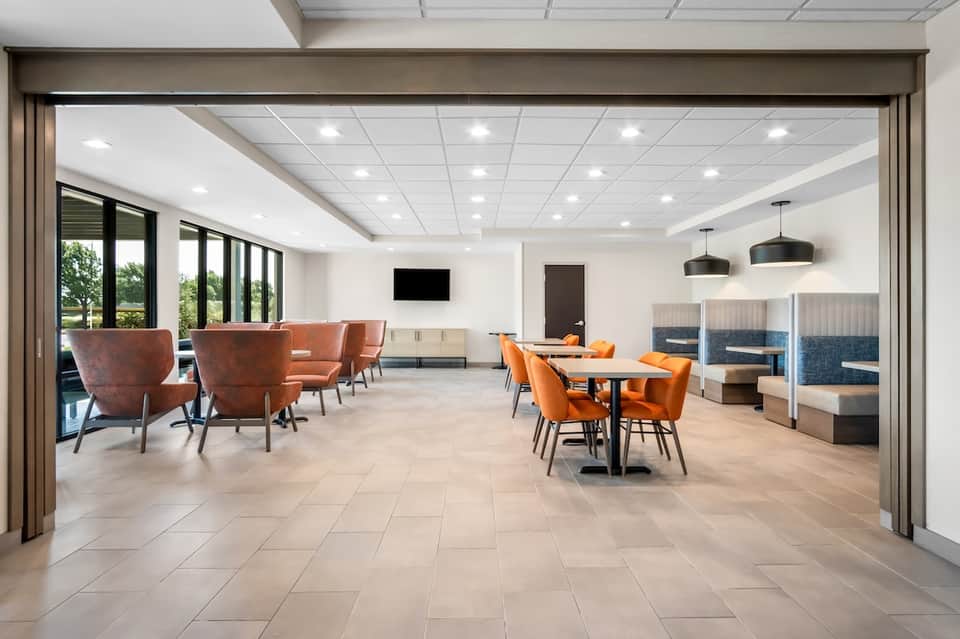 Contemporary hotel lounge with orange chairs, tables, and floor-to-ceiling windows