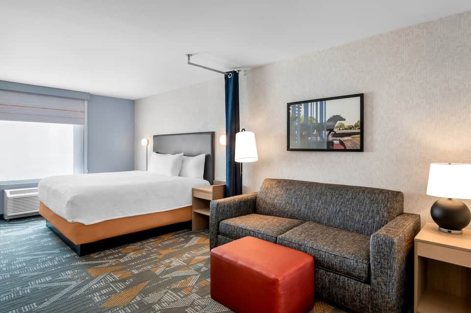 Modern hotel room with king bed, sofa, flat-screen TV, and contemporary decor