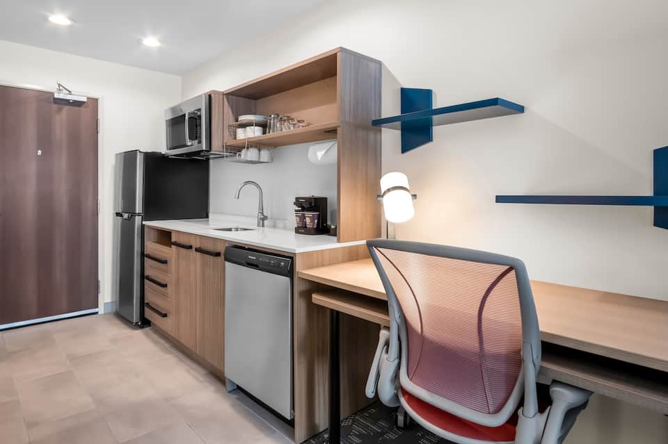 Contemporary studio apartment with kitchenette, work desk, and blue accent shelving