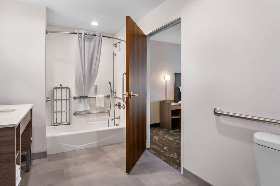 Hotel bathroom with white tile, walk-in shower with curtain, vanity, and accessibility grab bars
