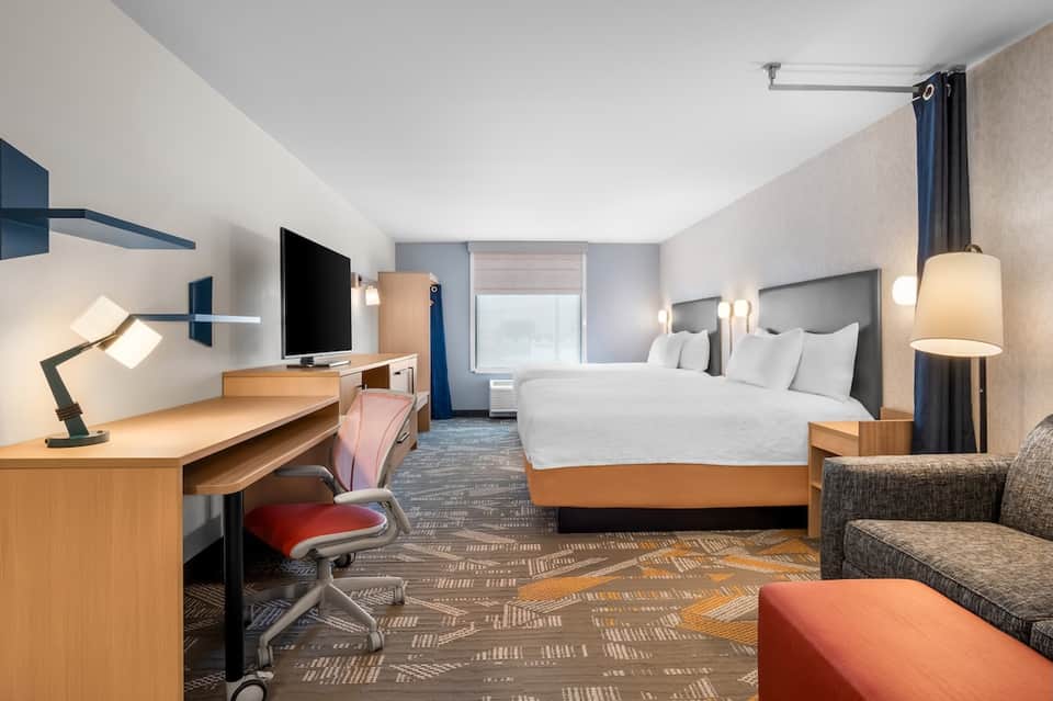 Contemporary hotel room with king bed, desk, TV, and colorful accent furnishings