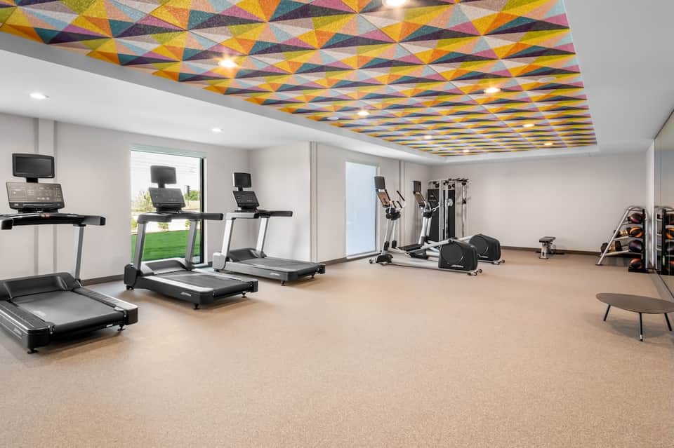 Bright fitness center with geometric ceiling, treadmills, exercise equipment, and natural light